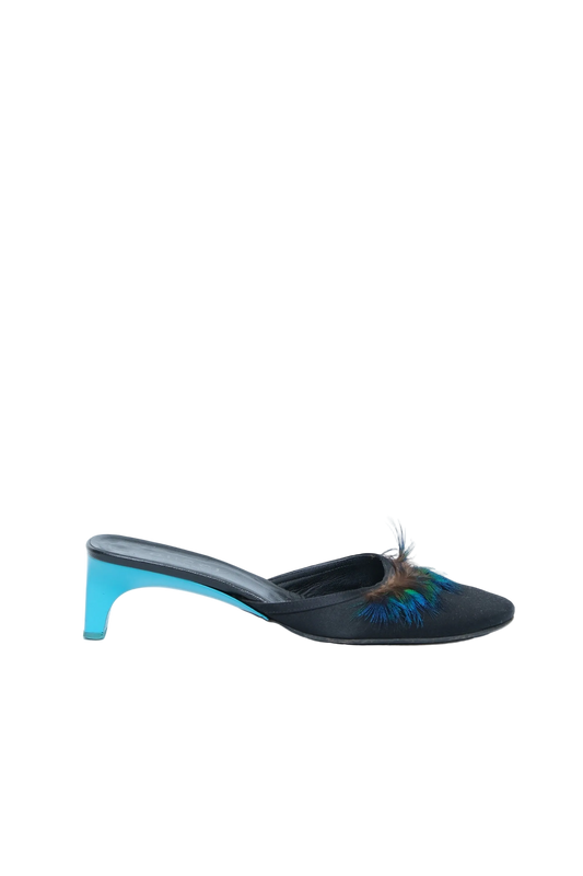 A single black mule sandal with a pointed toe, decorated with a blue and brown feather accent, and featuring a bright turquoise blue block heel, shown against a plain white background.