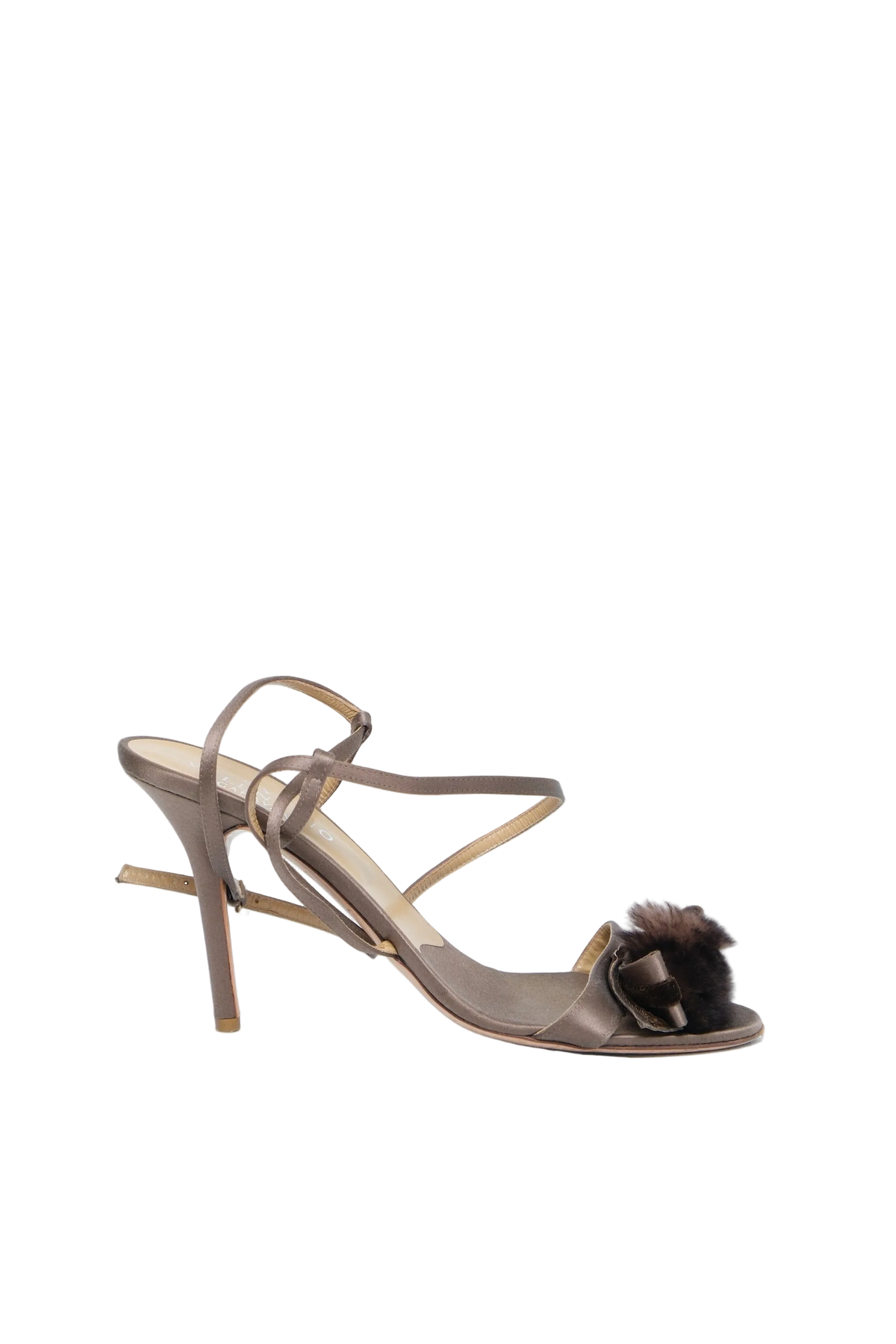 A single metallic taupe high-heeled sandal with thin wrap-around straps and a dark brown faux-fur pom-pom accent on the toe strap, shown against a light blue studio background.
