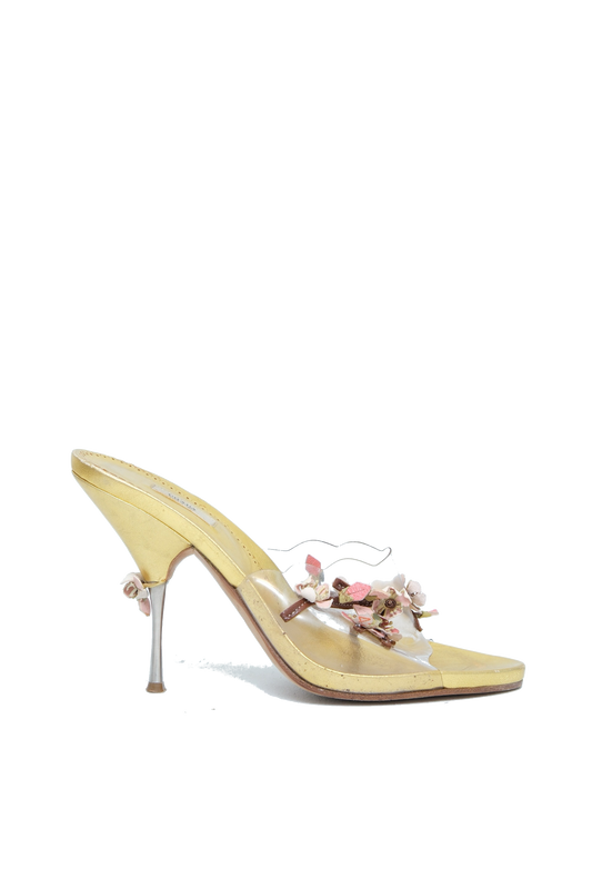 A pale yellow patent leather mule sandal with a pointed toe, a slim stiletto heel, and a decorative floral embellishment on the strap.