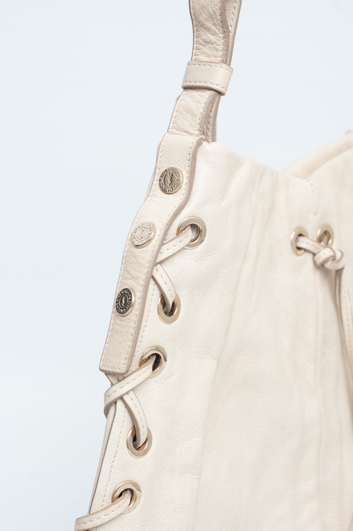 Close-up of a beige leather bag with decorative stitching and buttons on a light gray background